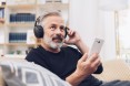 Mittelalter Mann mit Bart sitzt auf Sofa und hört Podcast
