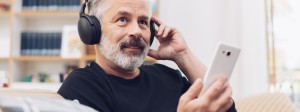 Mittelalter Mann mit Bart sitzt auf Sofa und hört Podcast