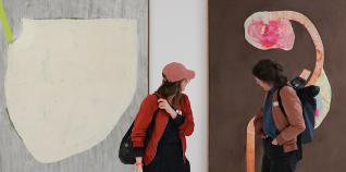 Im Hintergrund befinden sich zwei großformatige abstrakte Gemälde an einer weißen Wand. Im Vordergrund befinden sich zwei Personen, die eines der beiden Gemälde betrachten.