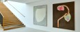 Zwei großformatige abstrakte Gemälde. Auf der linken Seite eine Holztreppe, die in den ersten Stock führt. Ein Gemälde ist in Grau- und Beigetönen gehalten. Das andere hat braune, pastellfarbene und fuchsiafarbene Töne. 
