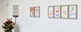 Mehrere abstrakte Gemälde an einer weißen Wand. Auf der linken Seite befindet sich eine künstlerische Installation, die aus einem umgedrehten Besen besteht, der ein abstraktes Gemälde hält.