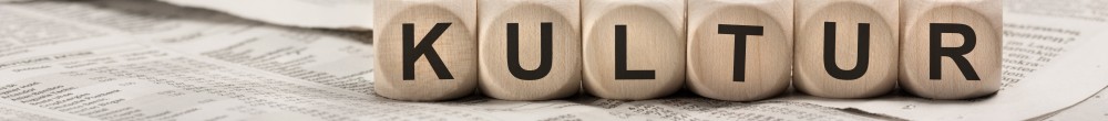 Buchstabenwürfel die das Wort Kultur ergeben liegen auf mehreren Zeitungsblättern. Der Fokus des Bildes liegt auf Kultur.