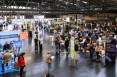 ca. 20 Beratertische mit anwesenden Beratern und Gründer*innen an den Tischen in der Messehalle. bild von oben auf die Halle.