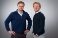 Zwei männliche Gründer als Teamfoto mit hellblauem Hintergrund.