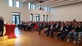 155 Gäste im Saal vor einem Podium mit dem Vorstandsvorsitzenden auf der Bühne und zwei roten Stehtischen