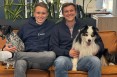 Lasse Steffen und Marco Kippler sitzen als Gründer mit blauen Hoodies auf einer Couch, schauen lachend in die Kamera  und haben beiden jeweils einen Hund im Arm.